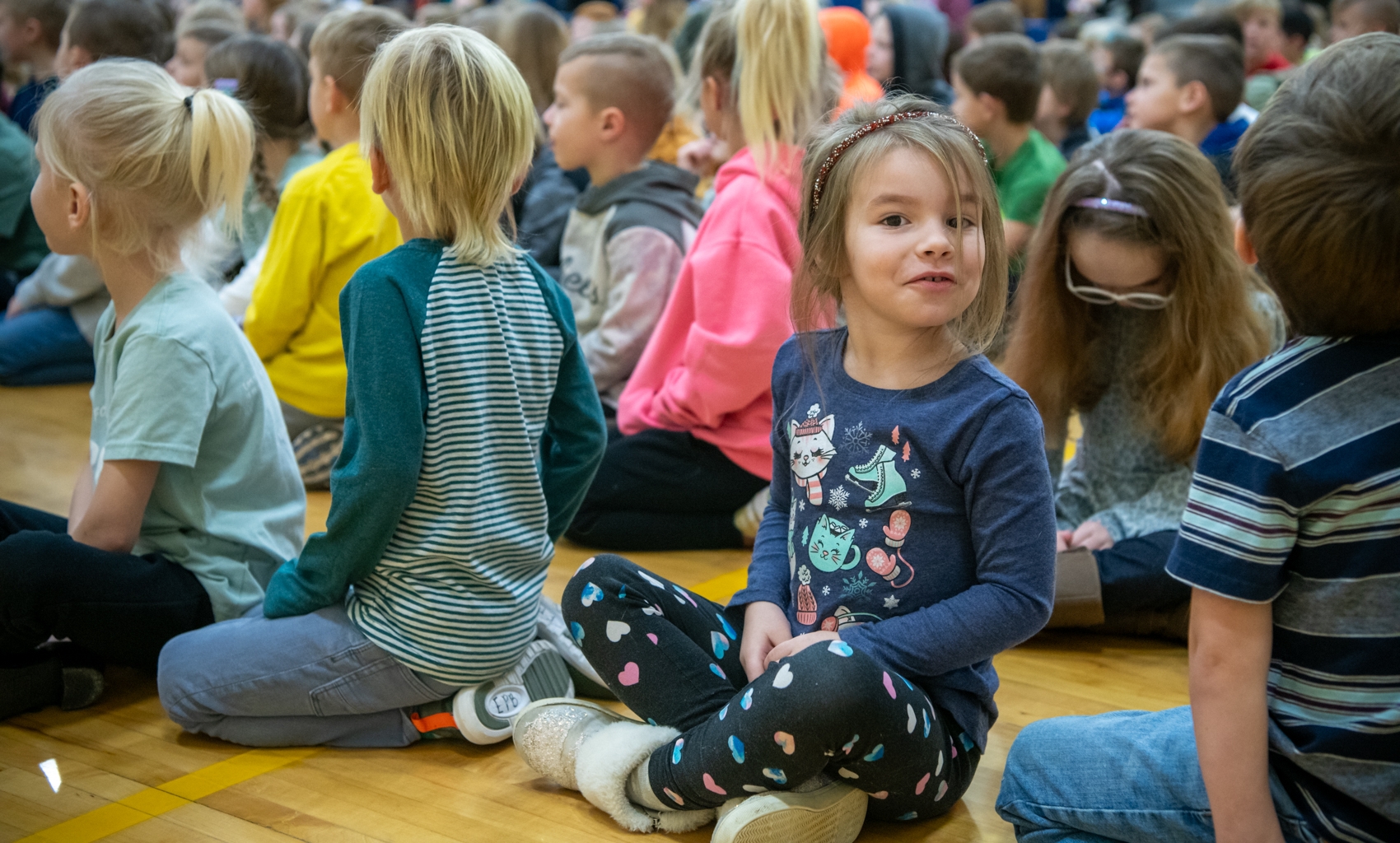 Little girls smiles at the camera during a chapel in the gym.