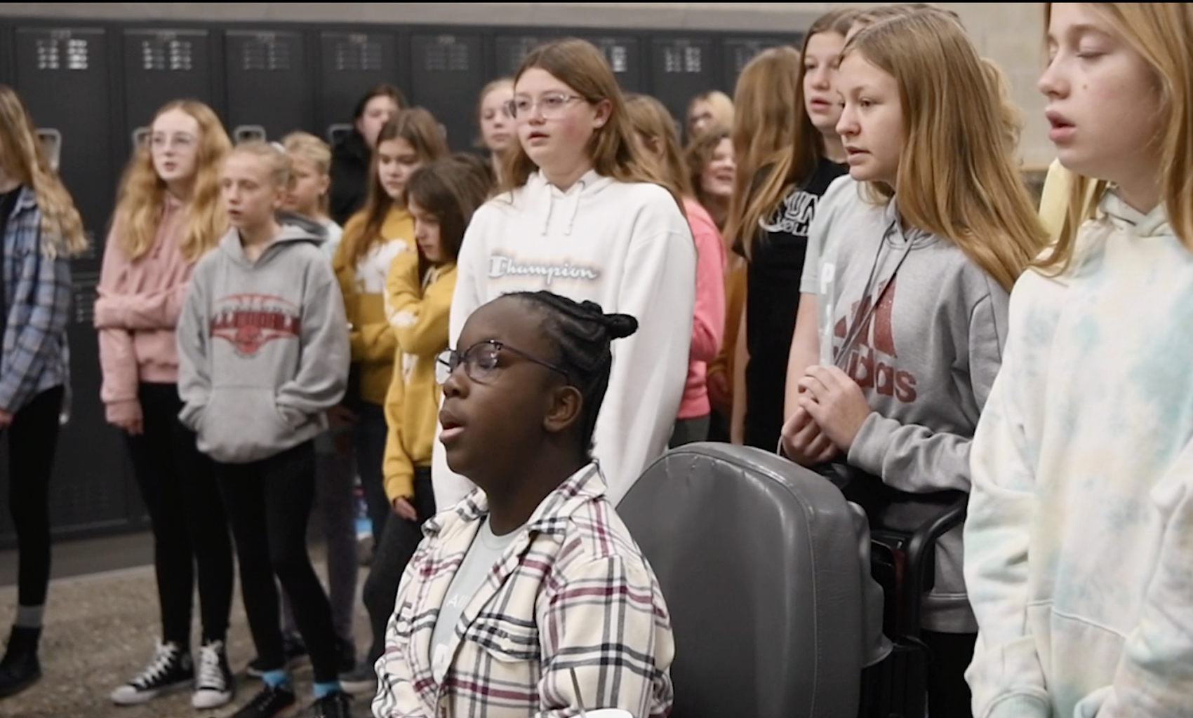 Girls standing in a semi-circle and singing with their eyes closed.